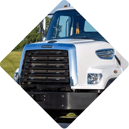 Detailed close-up of a white Freightliner 108SD Plus truck, capturing its bold grille and distinctive headlamps. Set against a verdant backdrop, the robust design and signature features of the truck exude reliability and strength. Ideal for diverse job sites, the Freightliner 108SD Plus combines both form and function, showcasing why it's a top choice for professionals in the industry.