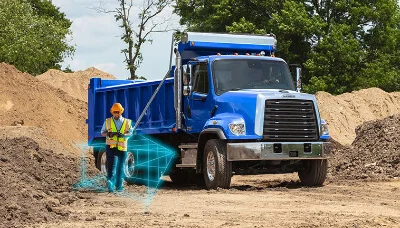 An imposing blue Freightliner 108SD Plus truck is stationed on a muddy construction site, surrounded by mounds of dirt. To its side stands a worker, adorned in a reflective safety vest and helmet, seemingly reviewing data or schematics from a holographic interface in front of him. The vivid holographic display emphasizes the cutting-edge safety technology and innovative solutions incorporated into the truck's operations. The clear presence of the safety-conscious worker in close proximity to the truck showcases the emphasis Freightliner places on ensuring the well-being of its operators. This image perfectly blends the raw power of the 108SD Plus with the advanced safety features it boasts, underlining its reputation as a trusted workhorse in challenging environments.