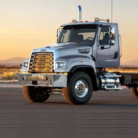 Freightliner 114SD truck showcased against a serene sunset backdrop, highlighting its robust front grille, sleek silver finish, and rugged design for heavy-duty tasks.