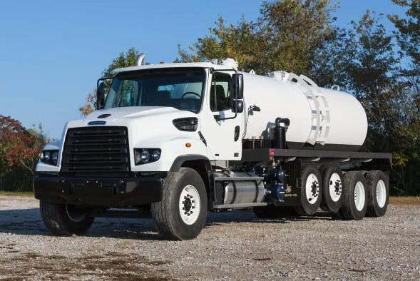 Freightliner 114SD Plus with large white tank on gravel ground near trees