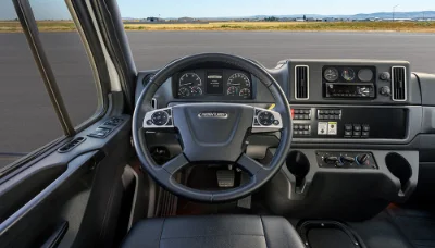Freightliner 114sd Plus truck interior showcasing detailed steering wheel, dashboard controls, and cabin view with airstrip background
