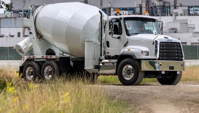 114sd Plus Freightliner white cement mixer truck parked on gravel with industrial background and wild grass foreground