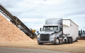 Freightliner Cascadia bulk haul truck with white trailer at a construction site with piles of material