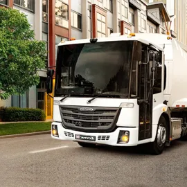 Efficient Freightliner EconicSD sanitation truck moving through an urban setting, with its modern design contrasting beautifully against the backdrop of city buildings and tree-lined streets.