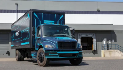 Freightliner eM2 electric truck parked outside a commercial building with blue and black detailing