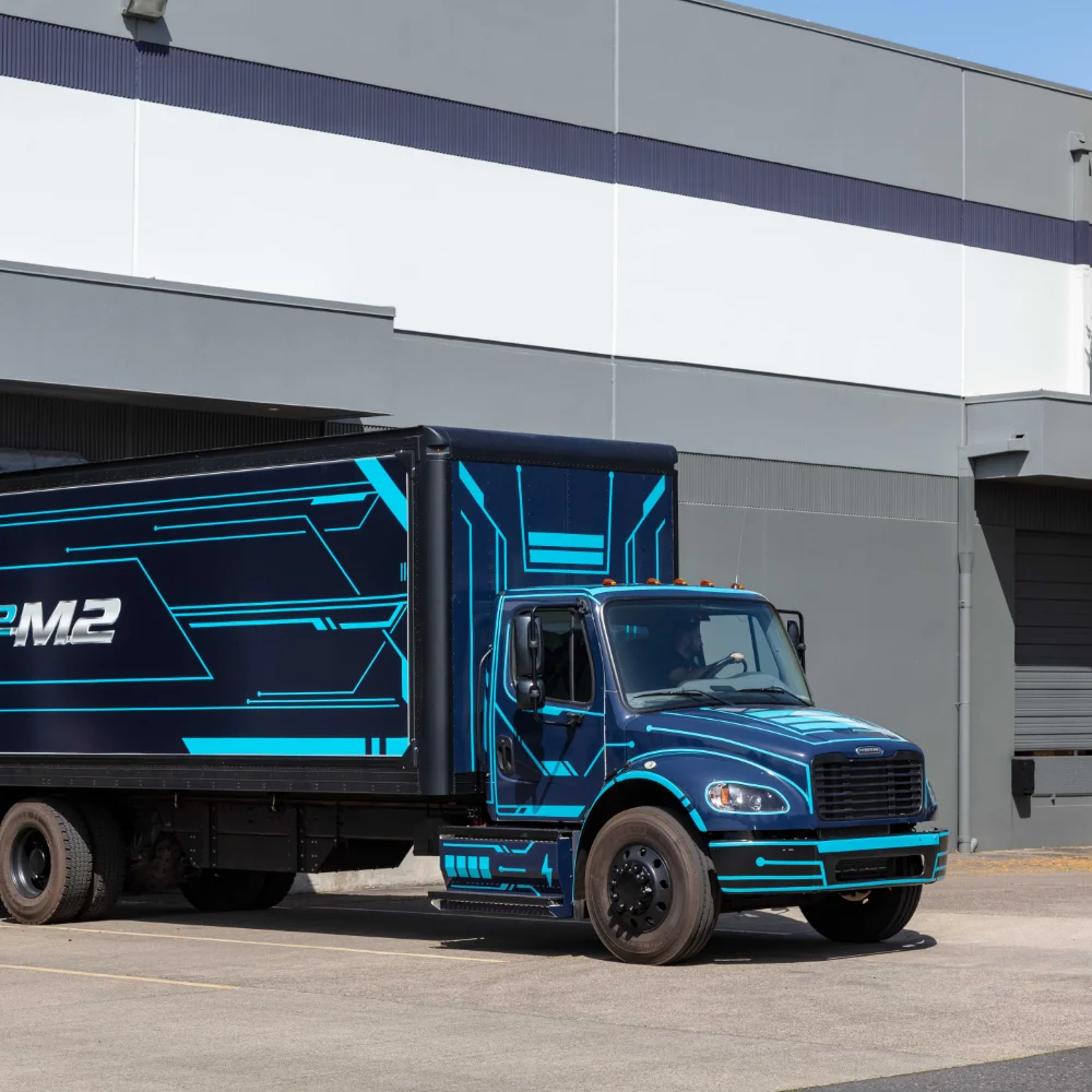 Freightliner eM2 electric truck in motion with urban building background and distinct blue graphics