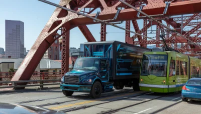 Freightliner eM2 electric truck driving near a tram on a city bridge