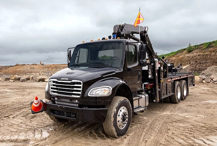 Freightliner M2 106 Plus black crane truck at a construction site with warning flags