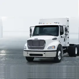Sleek Freightliner M2112 Natural Gas truck, showcasing its eco-friendly design, standing prominently against a minimalist backdrop. The vehicle's white hue contrasts with the gray surface, emphasizing its clean lines and modern aesthetics.