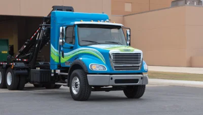 Blue Freightliner M2 112 Natural Gas truck with vibrant green stripes and a black equipment attachment parked outside a building