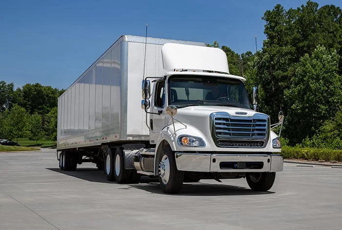 Freightliner M2 112 Plus Series truck with white trailer parked in a spacious lot