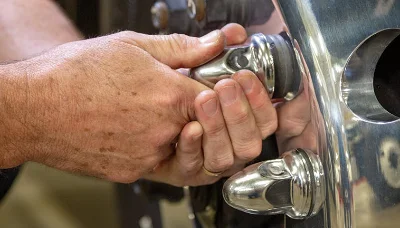 Technician hands adjusting chrome fittings on a Freightliner M2112 Plus Series truck wheel