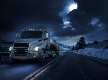 Freightliner tanker truck driving on a highway at night, symbolizing Francis Canada Truck Centre's 24/7 parts availability service.