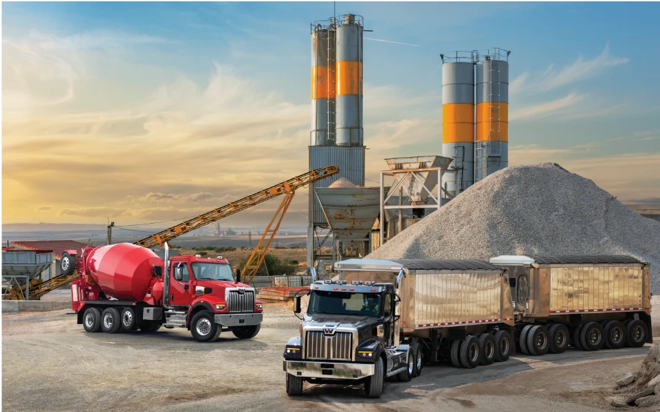 Red concrete mixer and silver Western Star 49x truck at a construction site with tall silos and gravel mound, Ottawa Ontario dealership
