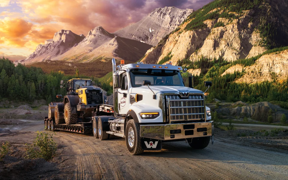 Western Star 49x white truck towing heavy machinery on rugged terrain with mountainous backdrop during sunset, Ottawa Ontario dealership
